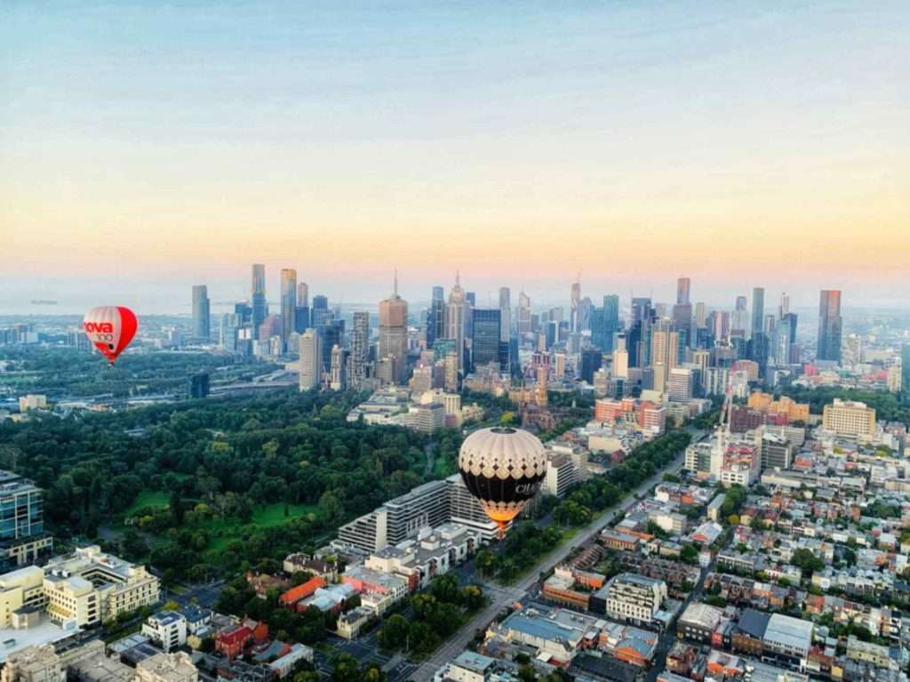 Hot air balloons floating over Melbourne city at sunrise with CBD skyline and parklands in background